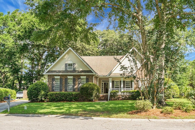 652 Spinner Cir, Mount Pleasant, SC 29464 - view of front of home with a front lawn, brick siding, covered porch, roof with shingles, and view of wooded area