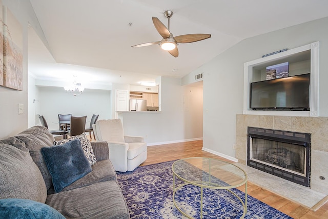 living room with hardwood / wood-style floors, lofted ceiling, ceiling fan with notable chandelier, and a fireplace