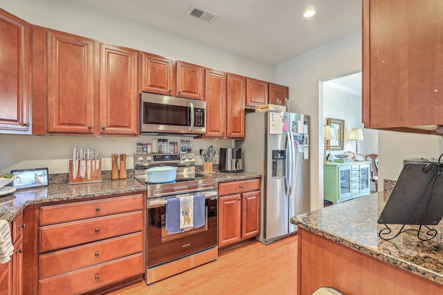 1723 Brittlebush Ln, Johns Island, SC 29455 - kitchen featuring appliances with stainless steel finishes, light wood-type flooring, dark stone countertops, brown cabinets, and recessed lighting