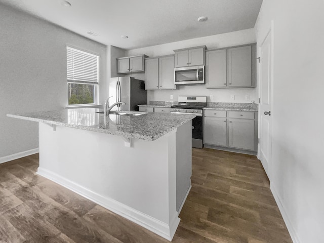 kitchen with an island with sink, a kitchen breakfast bar, light stone counters, and stainless steel appliances