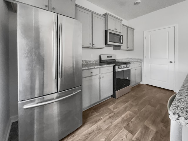 kitchen with light stone counters, appliances with stainless steel finishes, dark hardwood / wood-style flooring, and gray cabinets