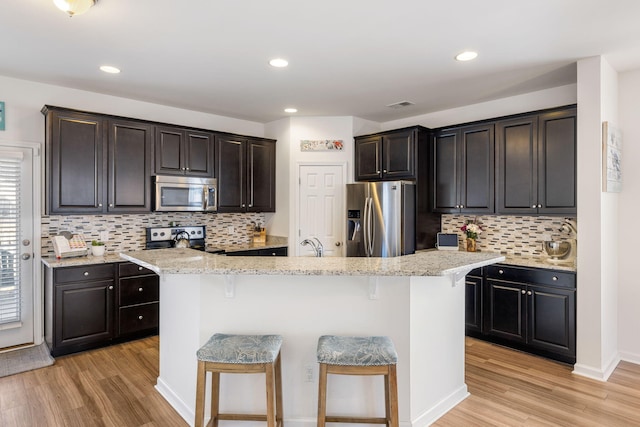 kitchen with light wood-type flooring, a kitchen breakfast bar, and appliances with stainless steel finishes