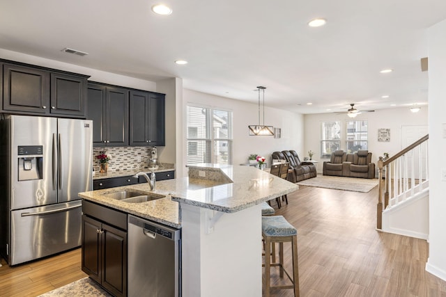 kitchen featuring visible vents, an island with sink, a sink, open floor plan, and appliances with stainless steel finishes