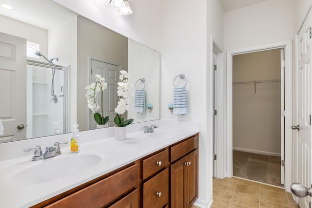 bathroom featuring a walk in closet, double vanity, a stall shower, tile patterned floors, and a sink