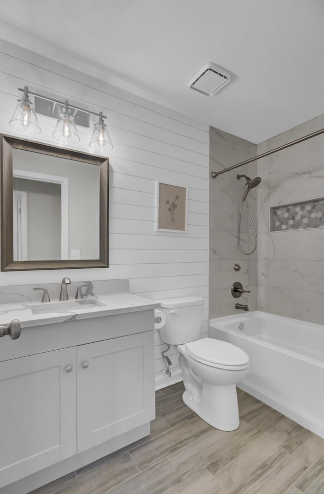 full bathroom featuring wood-type flooring, toilet, wooden walls, tiled shower / bath, and vanity