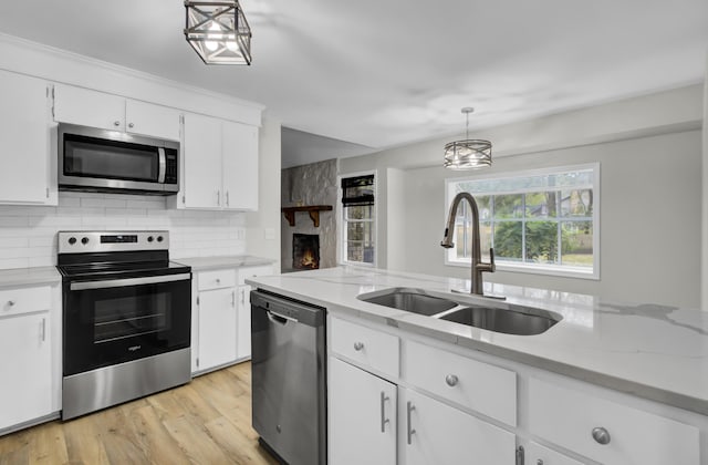 kitchen featuring appliances with stainless steel finishes, white cabinetry, light wood-type flooring, pendant lighting, and sink