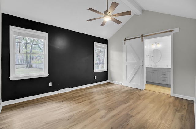 unfurnished bedroom with ensuite bathroom, multiple windows, light hardwood / wood-style flooring, and a barn door