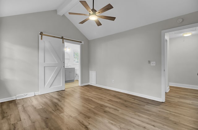 spare room with a barn door, vaulted ceiling with beams, light hardwood / wood-style floors, and ceiling fan