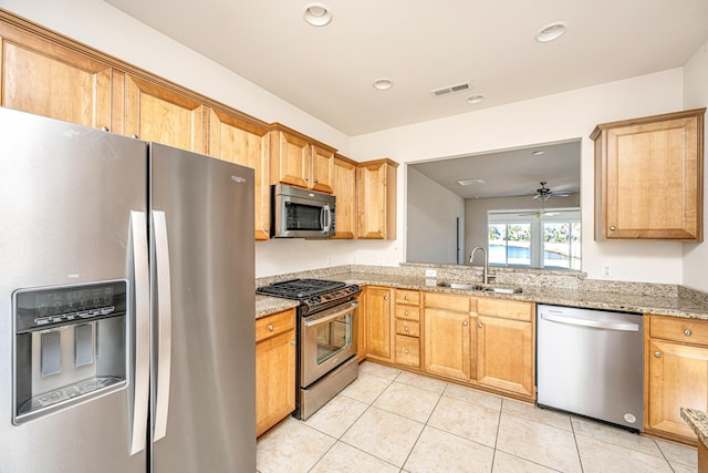 kitchen with light tile patterned floors, ceiling fan, stainless steel appliances, light stone countertops, and sink