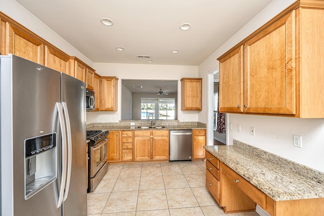 kitchen with light stone countertops, appliances with stainless steel finishes, sink, ceiling fan, and light tile patterned floors