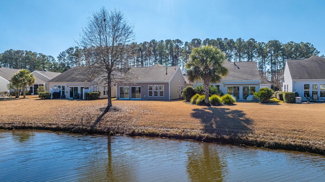 rear view of house with french doors, a lawn, and a water view