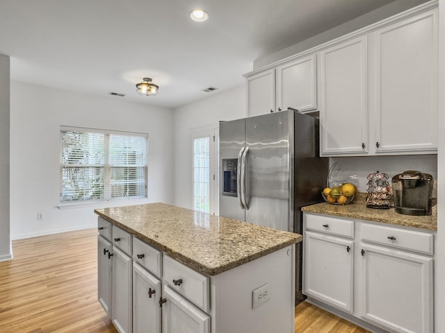 kitchen featuring light stone counters, light wood-style flooring, a kitchen island, visible vents, and stainless steel refrigerator with ice dispenser