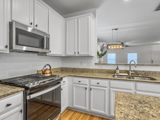 kitchen featuring stainless steel microwave, a sink, gas range, and white cabinets