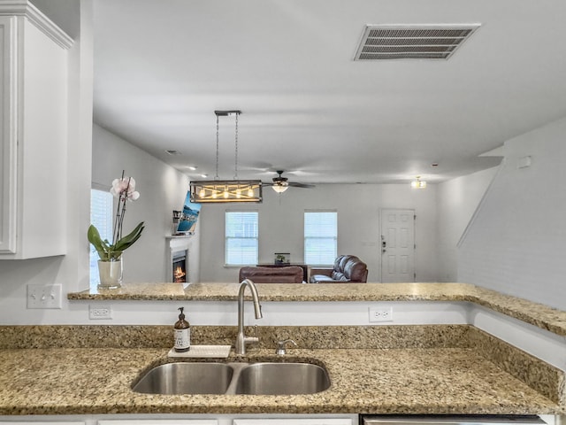 kitchen with visible vents, white cabinets, a sink, light stone countertops, and a lit fireplace