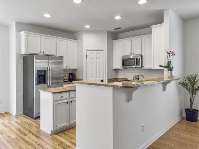 kitchen with a peninsula, visible vents, white cabinets, appliances with stainless steel finishes, and light stone countertops