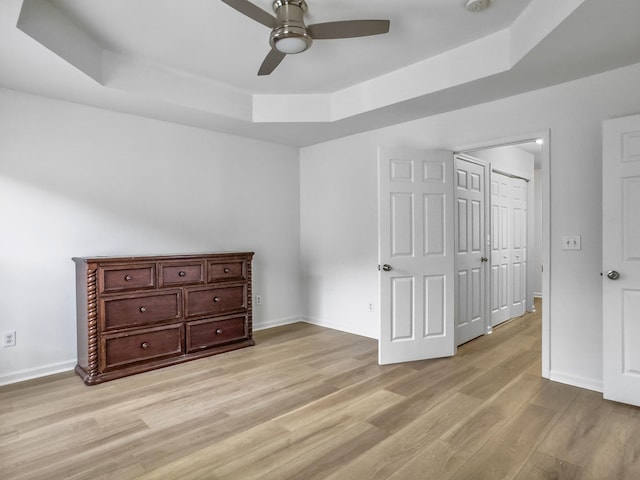 bedroom featuring a ceiling fan, a raised ceiling, light wood-style flooring, and baseboards