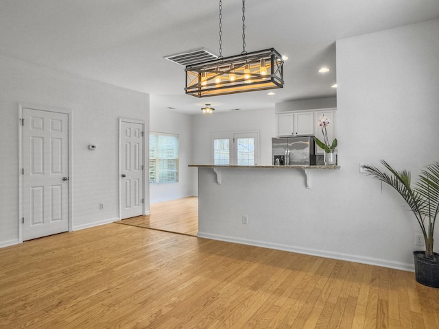 kitchen with hanging light fixtures, light wood-style flooring, white cabinetry, stainless steel fridge, and a kitchen bar