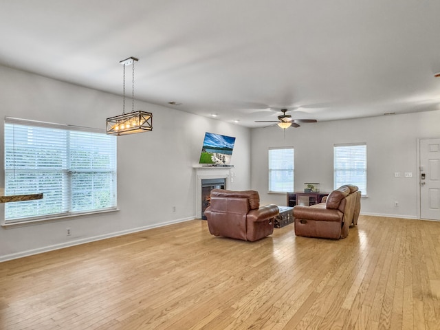 living area with a ceiling fan, light wood-type flooring, a lit fireplace, and baseboards