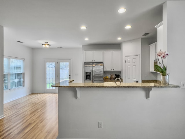 kitchen featuring a peninsula, a breakfast bar area, stone countertops, and stainless steel fridge