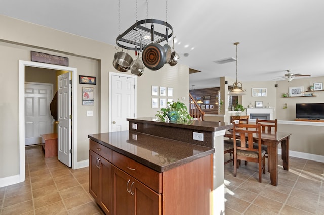 kitchen featuring a kitchen island, dark stone counters, hanging light fixtures, light tile patterned floors, and ceiling fan