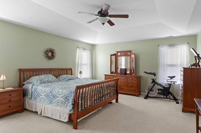 carpeted bedroom featuring multiple windows, a raised ceiling, and ceiling fan