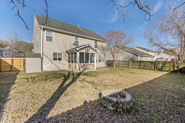 rear view of property with a storage shed, a lawn, a sunroom, and an outdoor fire pit