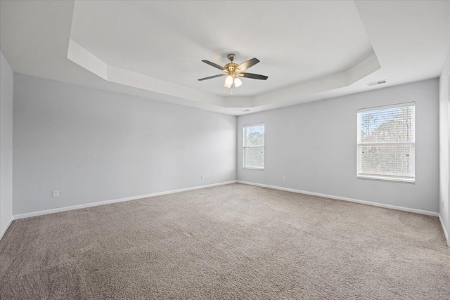 unfurnished room featuring ceiling fan, a healthy amount of sunlight, and a tray ceiling