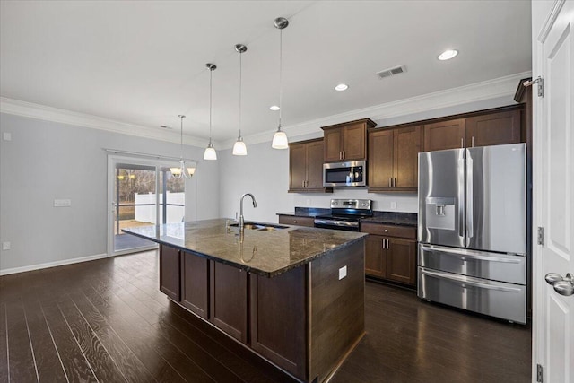 kitchen with decorative light fixtures, dark stone countertops, a center island with sink, sink, and stainless steel appliances