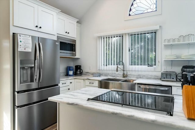 kitchen with white cabinets, sink, vaulted ceiling, light stone countertops, and appliances with stainless steel finishes