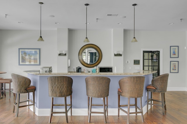 kitchen with hardwood / wood-style floors, a breakfast bar, visible vents, and baseboards