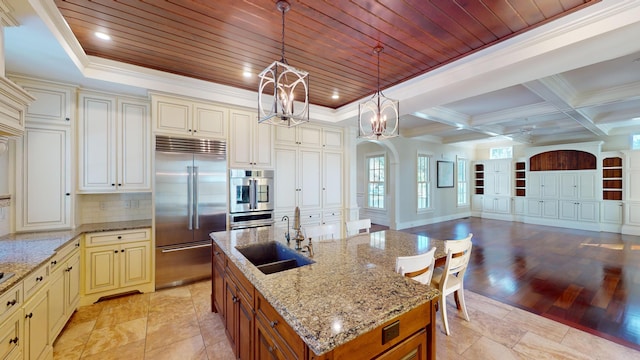 kitchen with pendant lighting, sink, a kitchen island with sink, stainless steel appliances, and cream cabinets