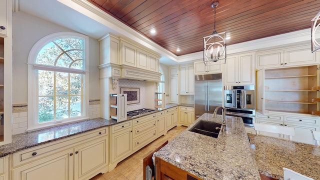 kitchen featuring decorative light fixtures, dark stone countertops, appliances with stainless steel finishes, a tray ceiling, and cream cabinets