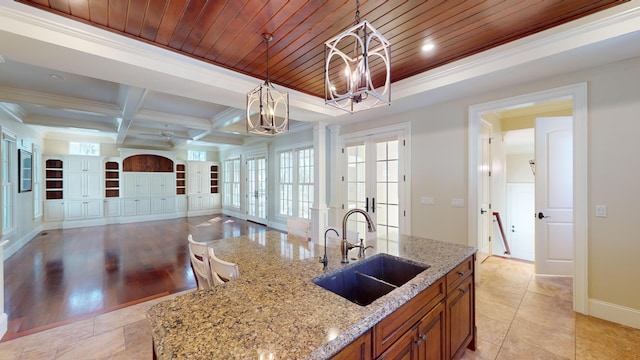 kitchen featuring sink, light stone counters, decorative light fixtures, wooden ceiling, and french doors