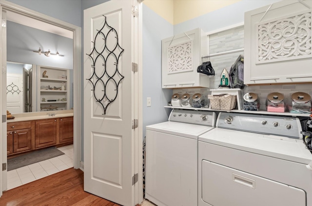 clothes washing area featuring hardwood / wood-style flooring, washing machine and clothes dryer, and cabinets