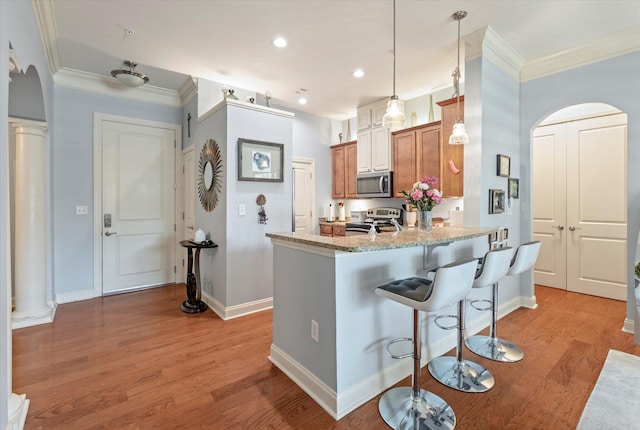 kitchen with light stone countertops, appliances with stainless steel finishes, kitchen peninsula, and light hardwood / wood-style flooring