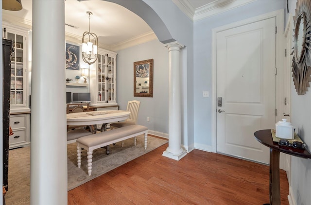 entrance foyer featuring a notable chandelier, hardwood / wood-style flooring, crown molding, and ornate columns