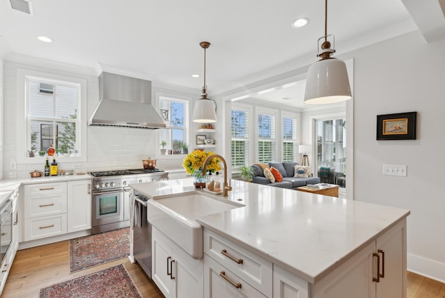kitchen with visible vents, light wood-style floors, wall chimney exhaust hood, a sink, and stainless steel appliances