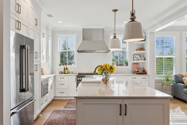 kitchen with wall chimney range hood, a center island, tasteful backsplash, high end refrigerator, and light wood finished floors