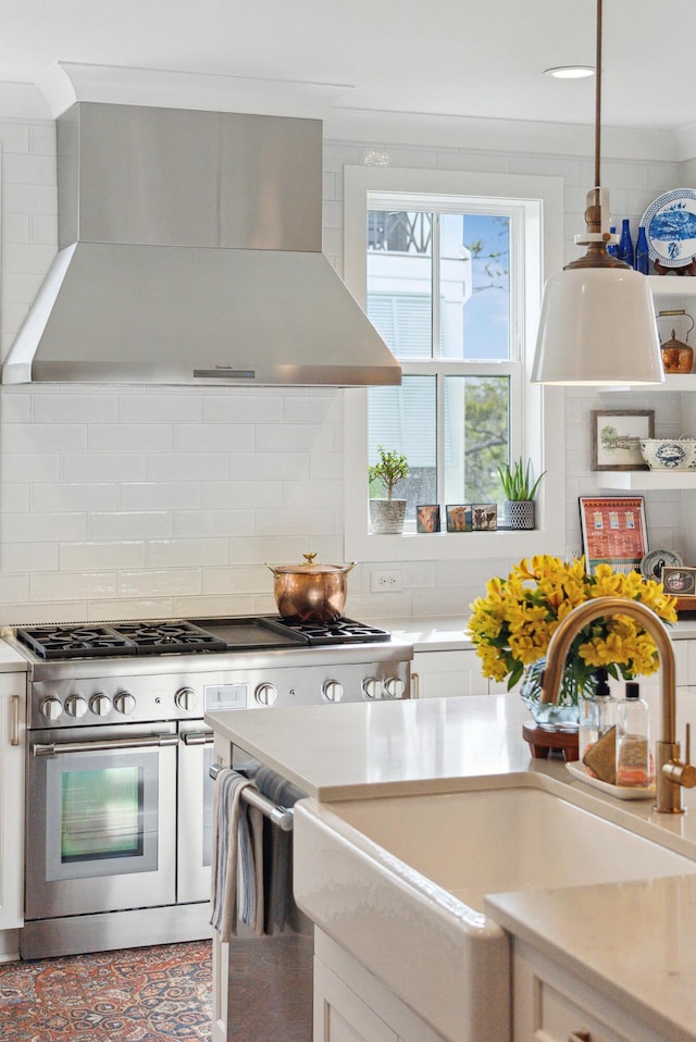 kitchen featuring wall chimney range hood, backsplash, appliances with stainless steel finishes, a sink, and white cabinetry