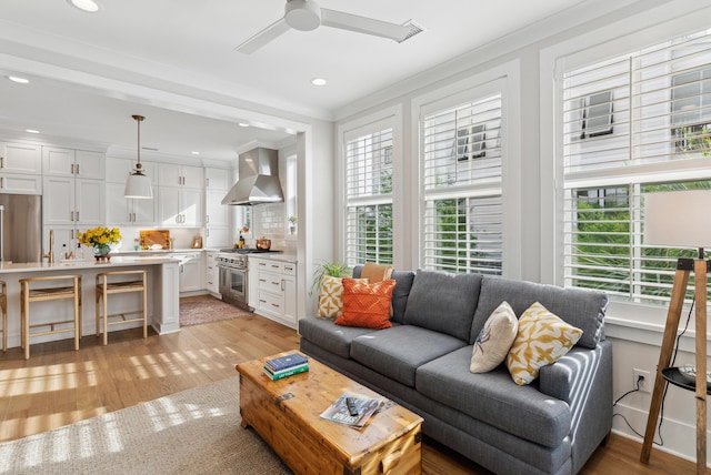 living room with crown molding, a ceiling fan, light wood-style flooring, and a wealth of natural light