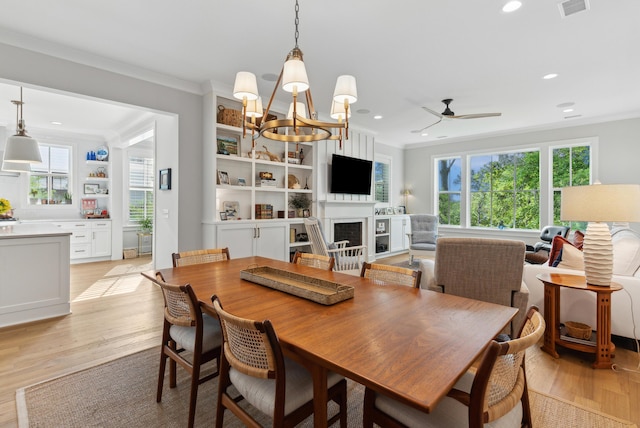 dining space with crown molding, a fireplace, recessed lighting, light wood-style flooring, and ceiling fan with notable chandelier