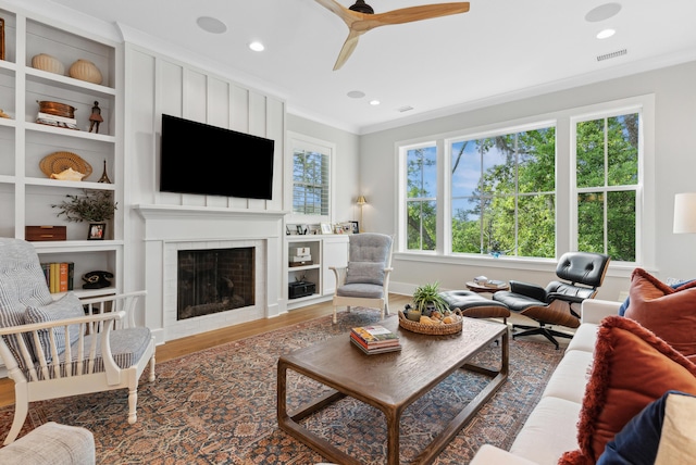 living area with crown molding, visible vents, wood finished floors, a fireplace, and a ceiling fan