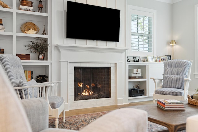 living area with built in shelves, a fireplace, and wood finished floors
