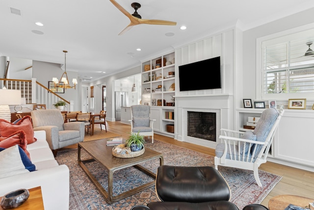living room featuring crown molding, a fireplace, ceiling fan with notable chandelier, recessed lighting, and wood finished floors