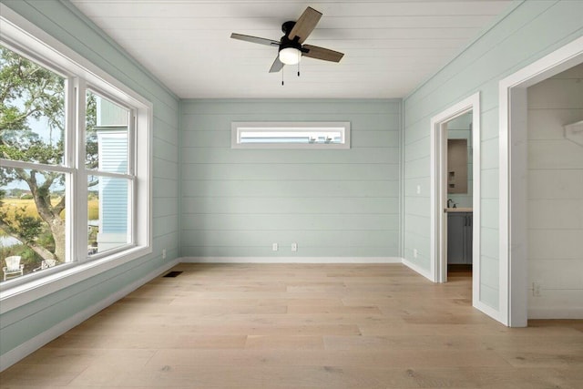 interior space with light wood-type flooring, wooden walls, and ceiling fan