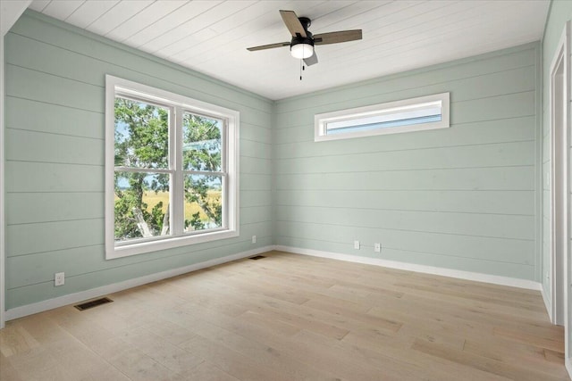 empty room featuring wooden walls, light hardwood / wood-style floors, and plenty of natural light