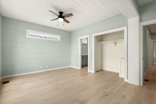 unfurnished bedroom featuring ceiling fan, wooden walls, a closet, and light hardwood / wood-style flooring