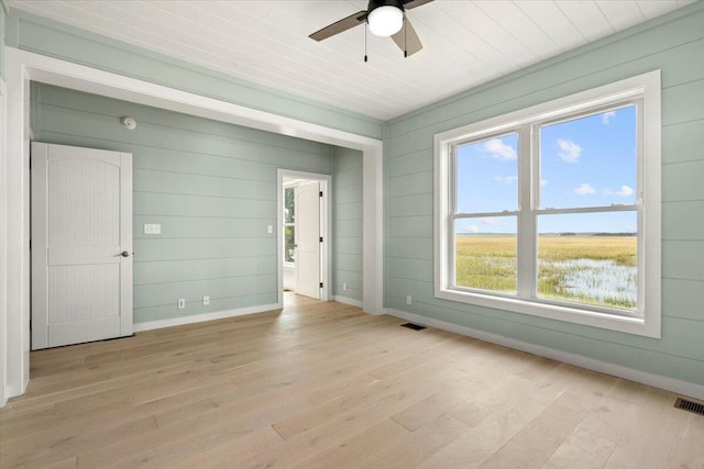 unfurnished room with light wood-type flooring, wooden walls, and ceiling fan