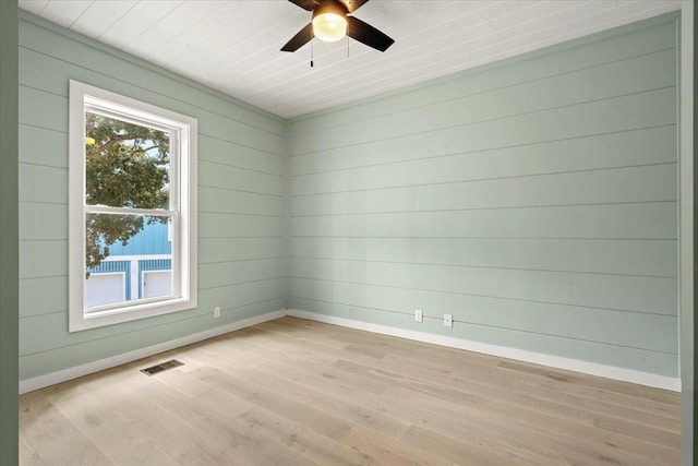 empty room with ceiling fan, wooden walls, and light hardwood / wood-style flooring