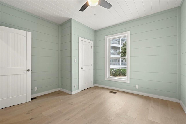 unfurnished bedroom featuring wood walls, light hardwood / wood-style floors, and ceiling fan